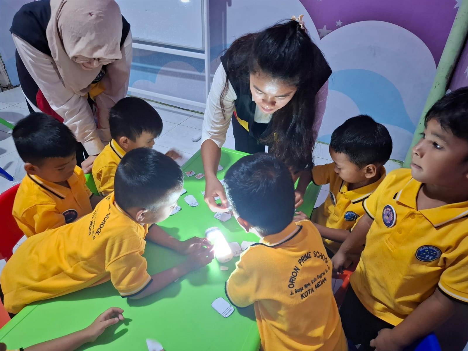 Anak-anak mengamati eksperimen cahaya di sekitar meja