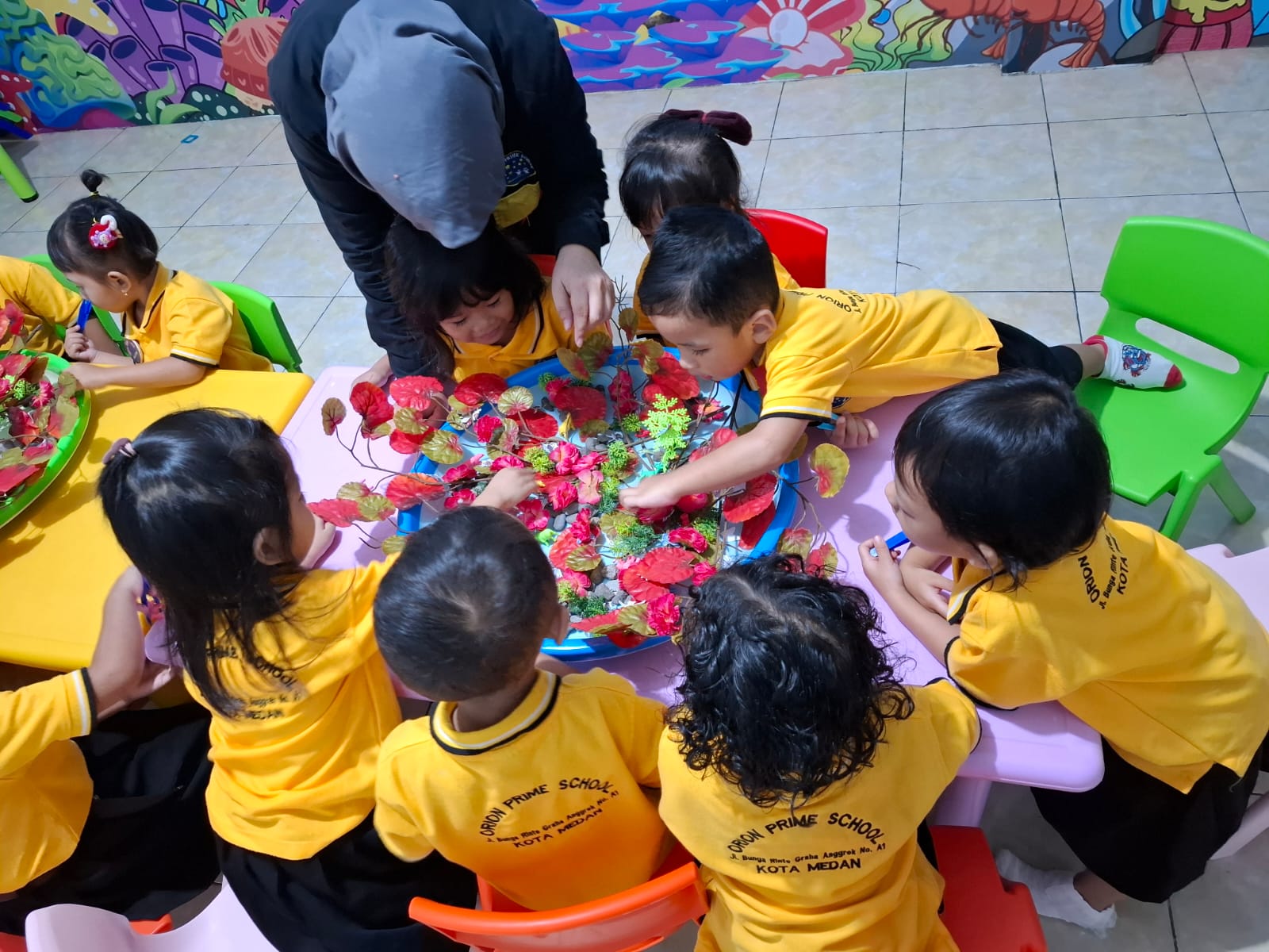 Anak-anak membuat kolase bunga bersama guru di meja kelas